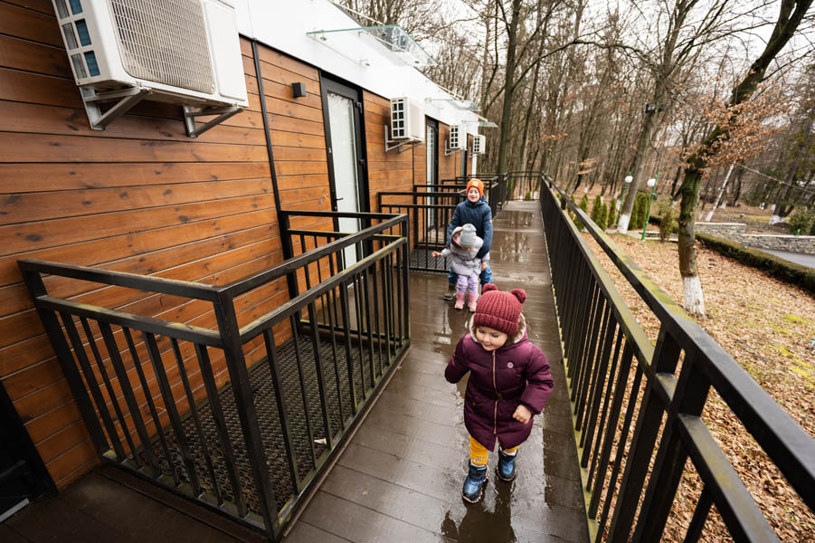What’s Next in Homebuilding? How Modular Homes Are Shaping the Future; Children walking on terrace of one-storey modular houses in spring rainy forest.
