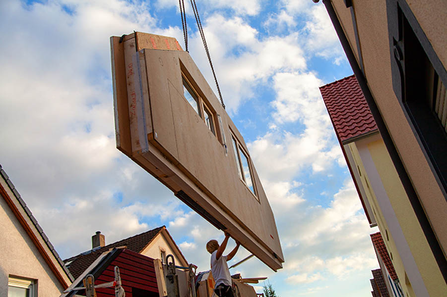 What to Expect During the Modular Home Building Process; A component with a sloping roof for a prefabricated house depends on the transport of a can and is brought into positions for lifting by the fitter