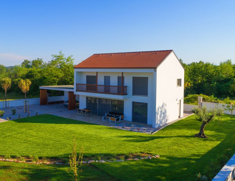 White modern home with red roof balcony and green lawn