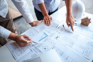 Architects reviewing house blueprints with model home and hard hat