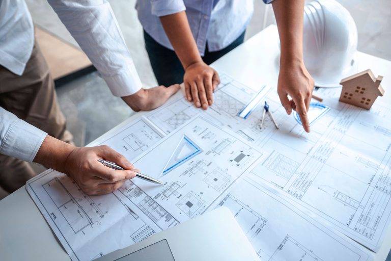 Architects reviewing house blueprints with model home and hard hat